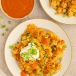 Buffalo Chicken and Rice on a plate with a dollop of greek yogurt on top and buffalo sauce on the side.