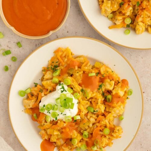 Buffalo Chicken and Rice on a plate with a dollop of greek yogurt on top and buffalo sauce on the side.