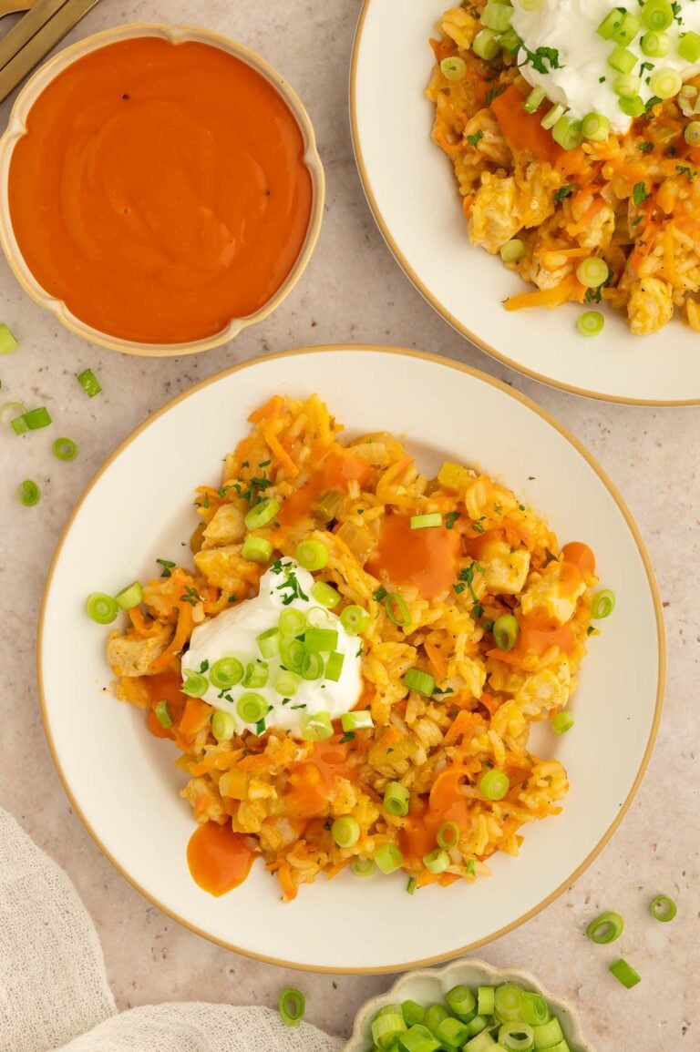 Buffalo Chicken and Rice on a plate with a dollop of greek yogurt on top and buffalo sauce on the side.