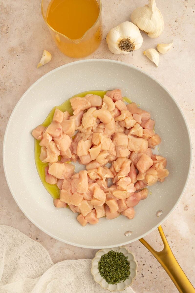 Cubed chicken and olive oil in a skillet on a counter.