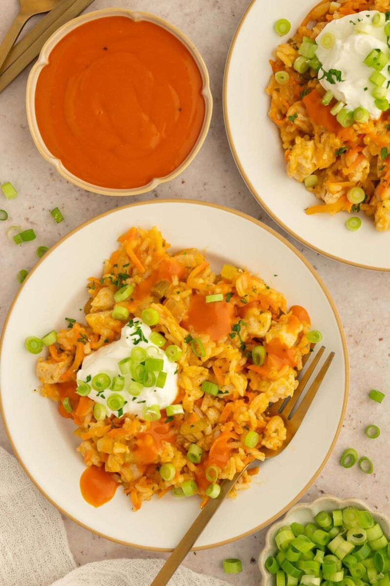 Buffalo Chicken and Rice on a plate with a dollop of greek yogurt on top and buffalo sauce on the side and a fork resting on the plate.
