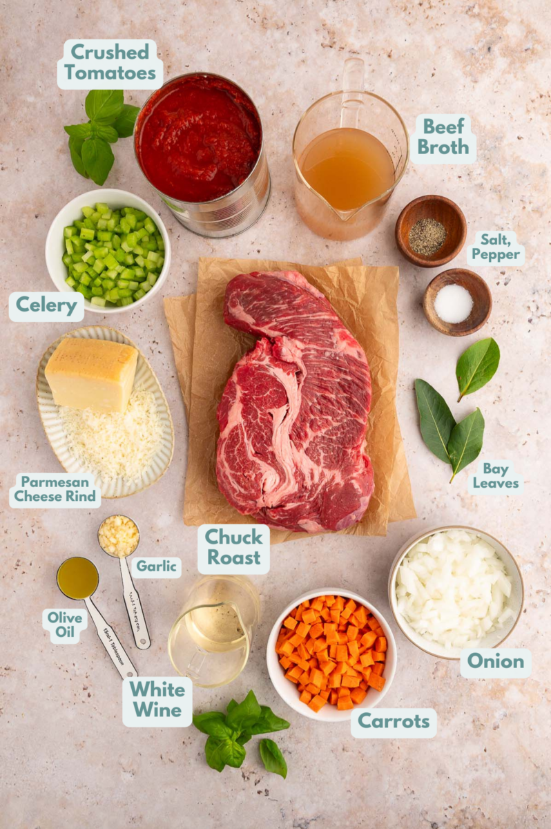 Ingredients for chuck roast pasta in small bowls: chuck roast, crushed tomatoes, beef broth, salt, pepper, bay leaves, onions, carrots, white wine, olive oil, garlic, parmesan cheese rind, celery.