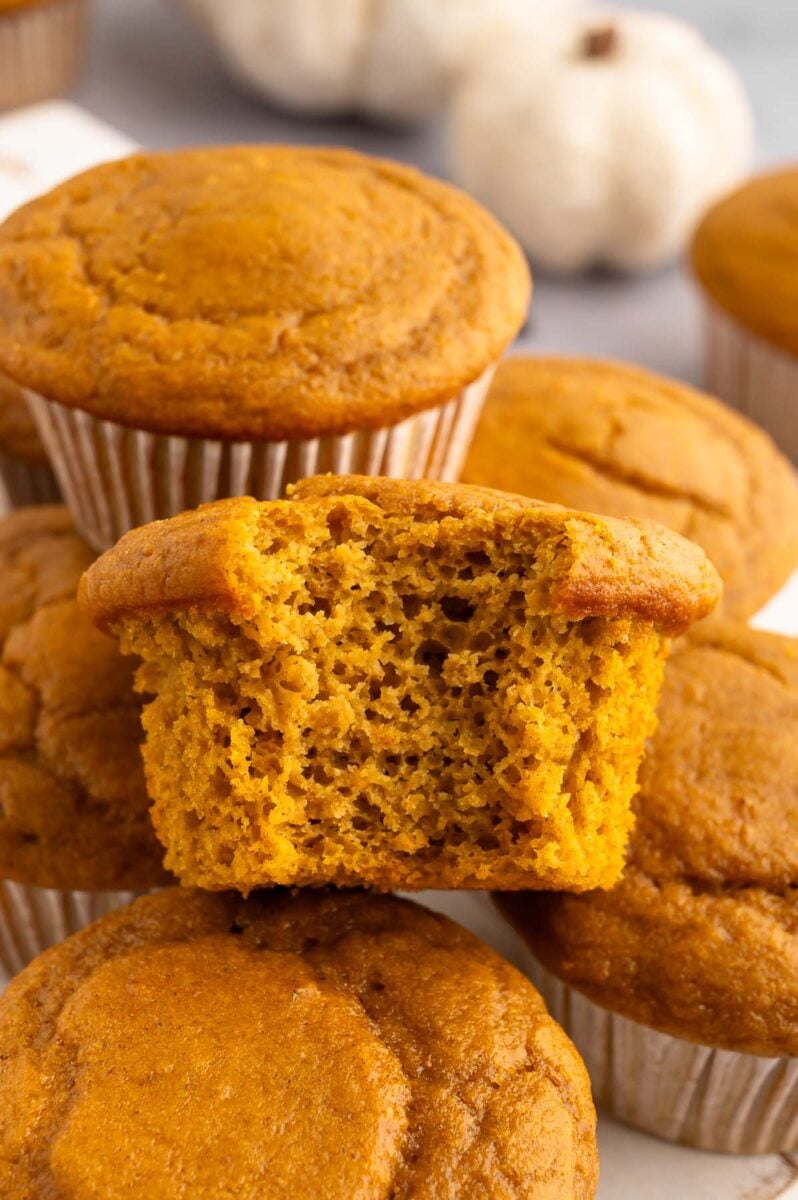 A pumpkin protein muffin with a bite taken out of it resting on more muffins.