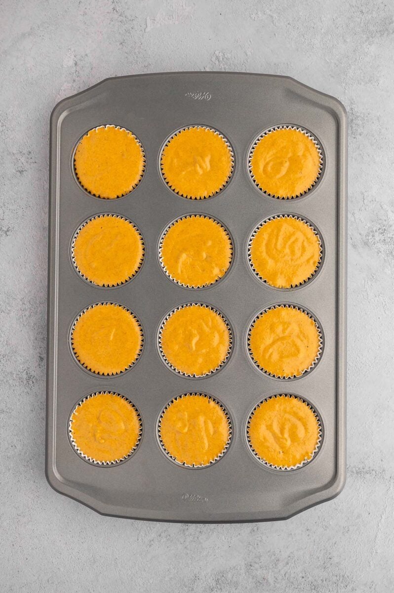 Uncooked pumpkin protein muffins in a muffin tin on a grey background.