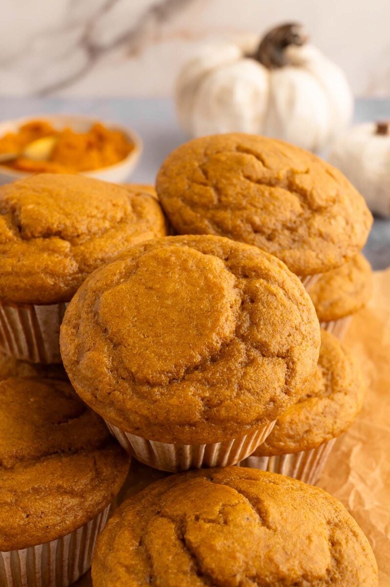 A pile of pumpkin protein muffins with a white pumpkin in the background.