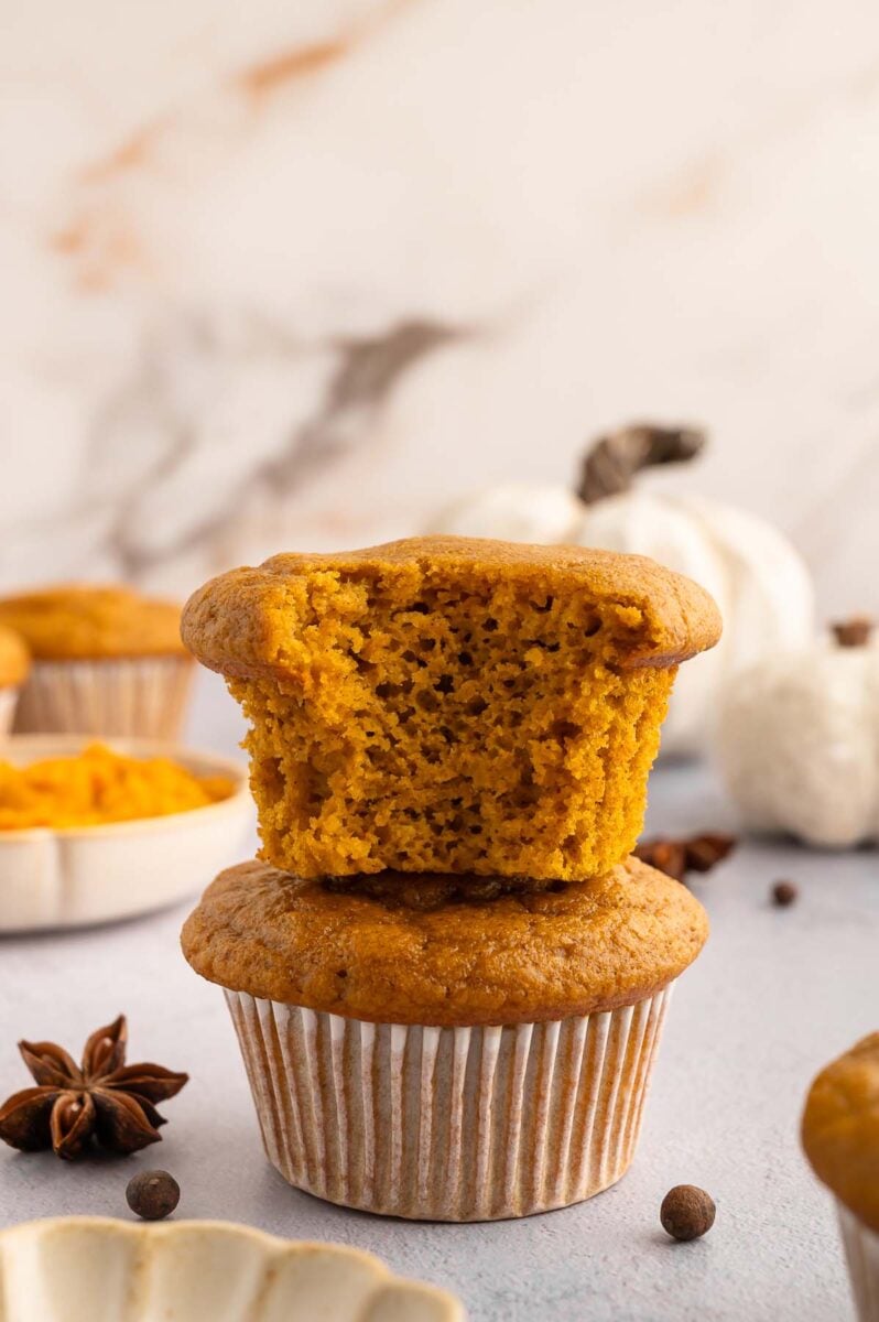 Two pumpkin protein muffins stacked on top of each other. The top has a bite taken out of it. 