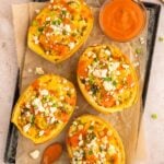 Buffalo Chicken Spaghetti Squash Boats on a parchment lined baking sheet with a bowl of buffalo sauce on the side.