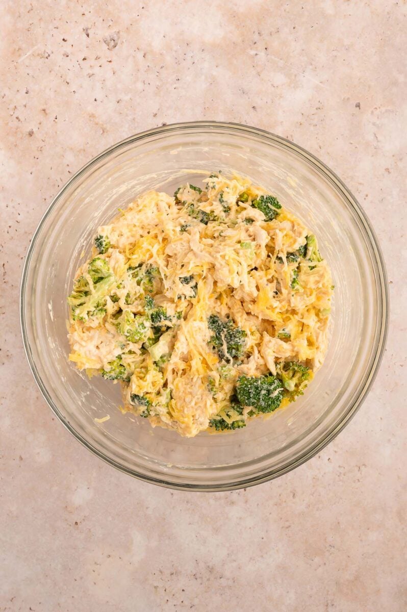 Cooked and shredded chicken, broccoli, hot sauce, yogurt and half the shredded cheese in a bowl.