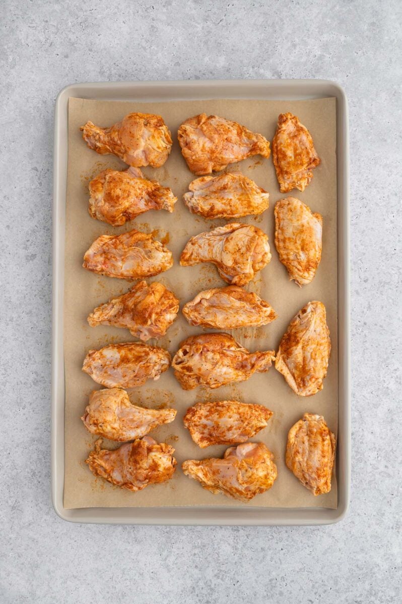 Uncooked pickle chicken wings on a parchment lined baking sheet.