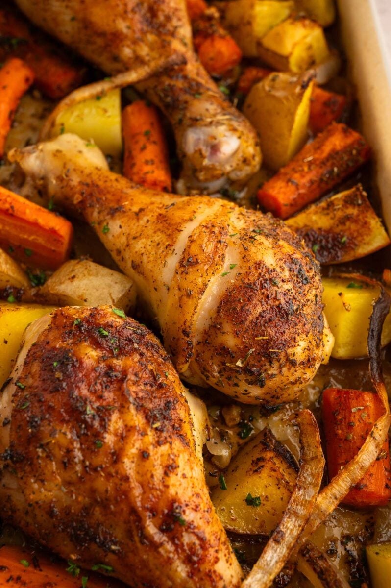 Chicken drumstick dinner with carrots and potatoes on a sheet pan.