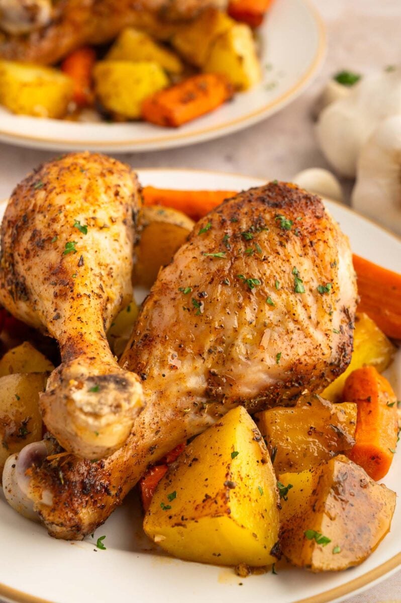 A close up of chicken drumstick dinner on top of potatoes and carrots.