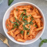 Healthy Penne Alla Vodka in a white bowl topped with fresh herbs and a fork on the side.