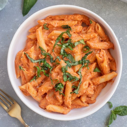 Healthy Penne Alla Vodka in a white bowl topped with fresh herbs and a fork on the side.