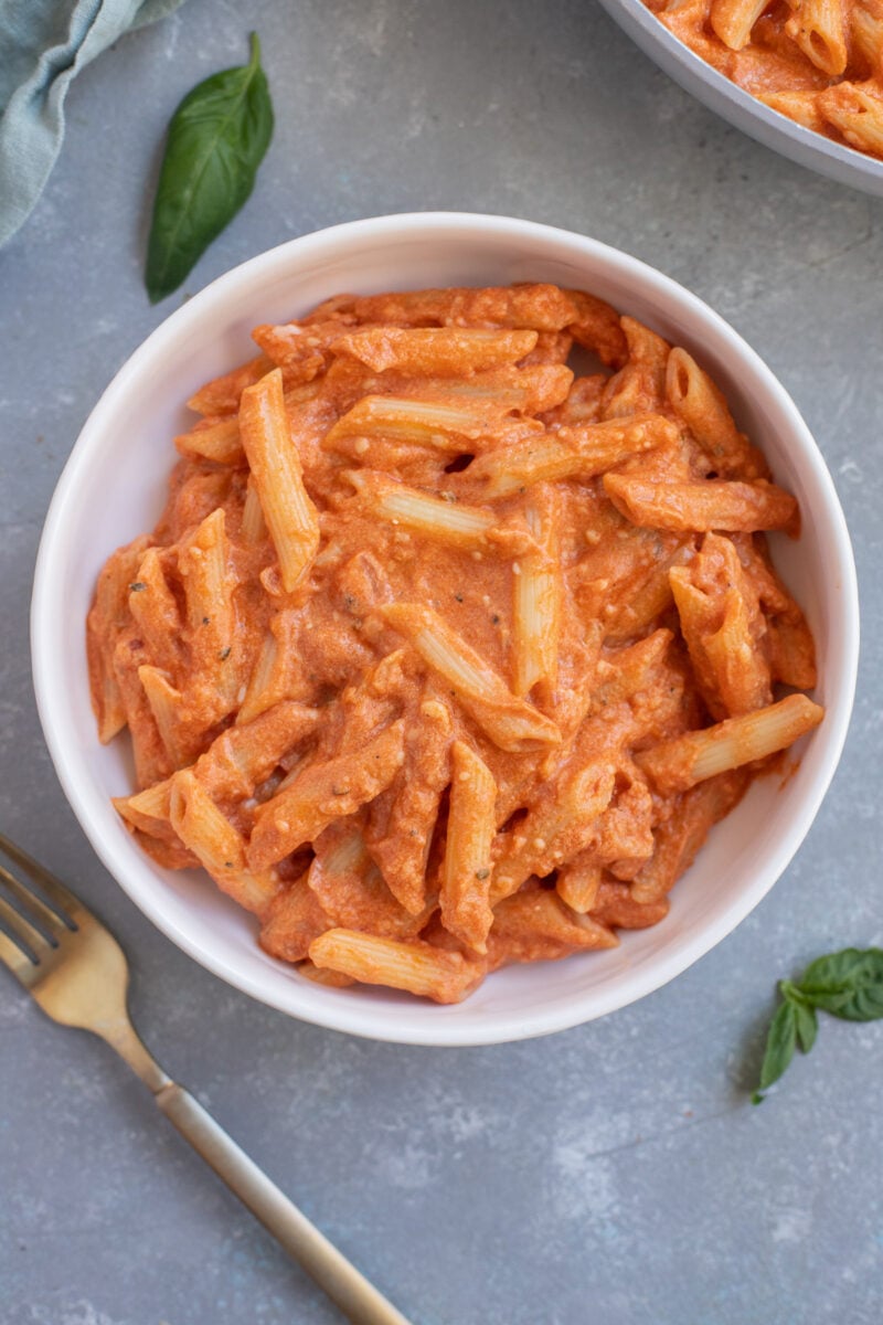 Healthy Penne Alla Vodka in a white bowl on a grey background with a gold fork.
