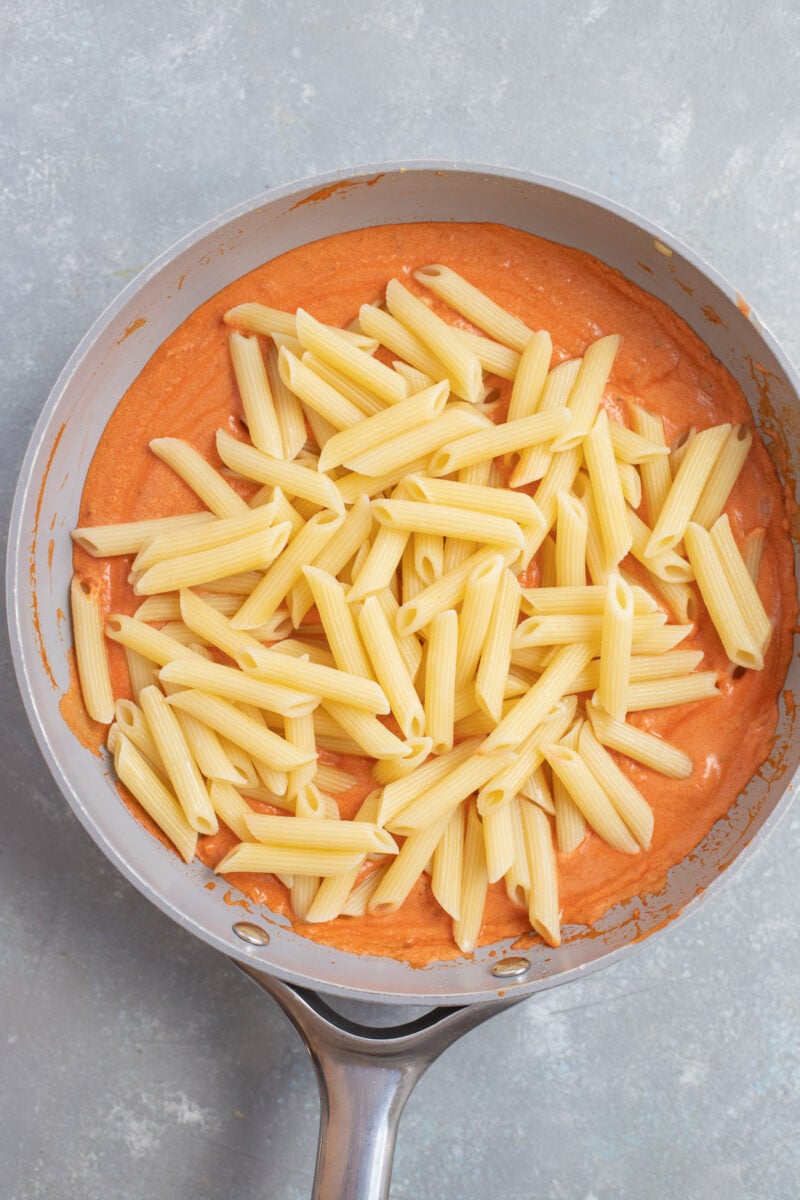 Penne pasta on top of vodka sauce in a saucepan on a grey background.