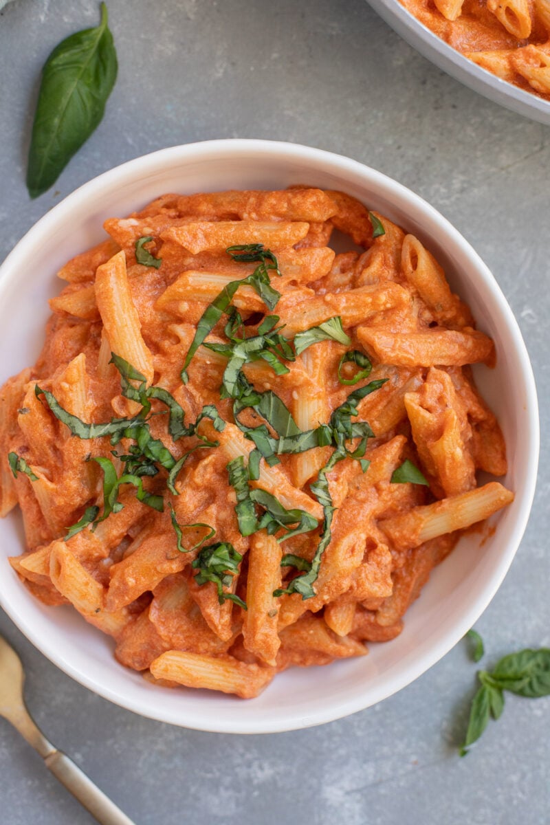 Healthy Penne Alla Vodka in a white bowl topped with fresh herbs.