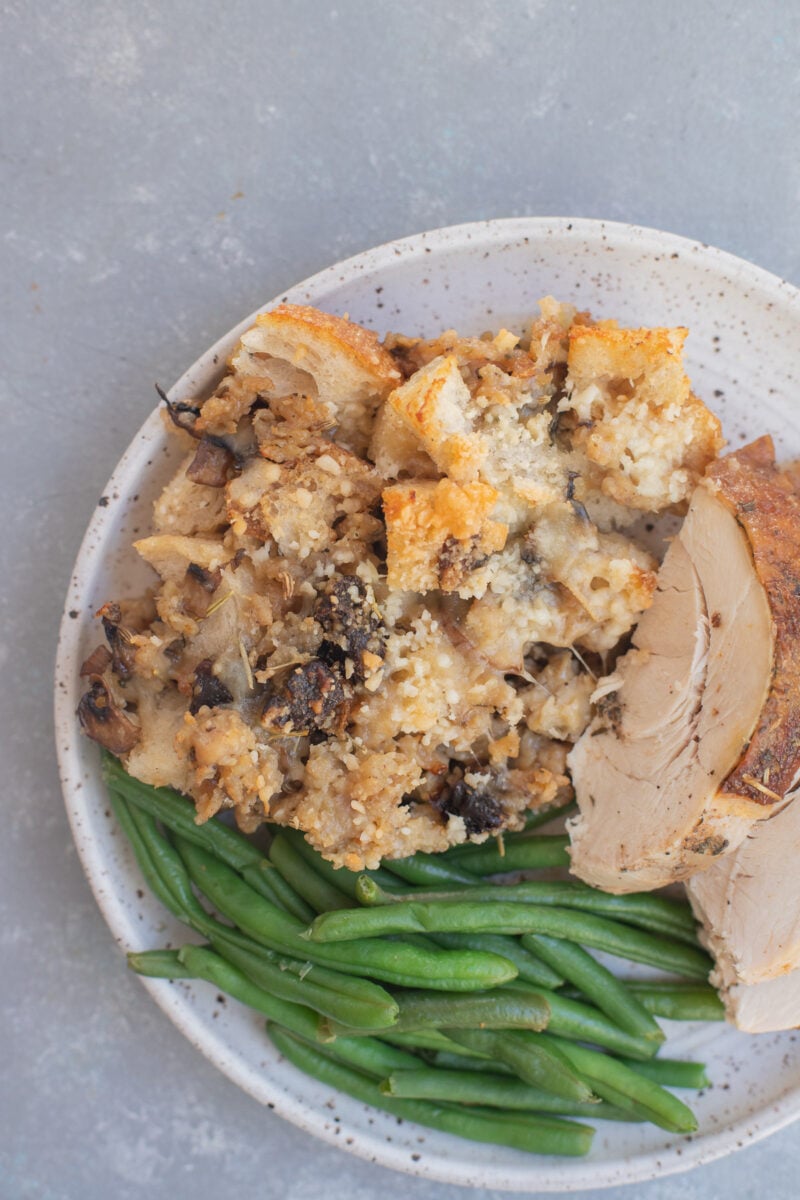 Sourdough sausage stuffing on a plate with sliced turkey and green beans.