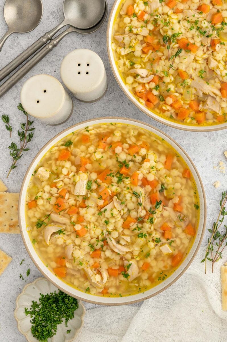 Chicken and Stars Soup in a bowl with another bowl of the soup and spoons on the side.