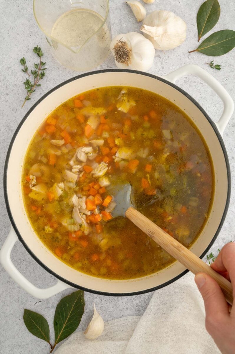 A spatula stirring chicken stars soup in a dutch oven before the pasta is added.