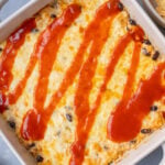 Chicken Enchilada Dip in a baking dish topped with more enchilada sauce.