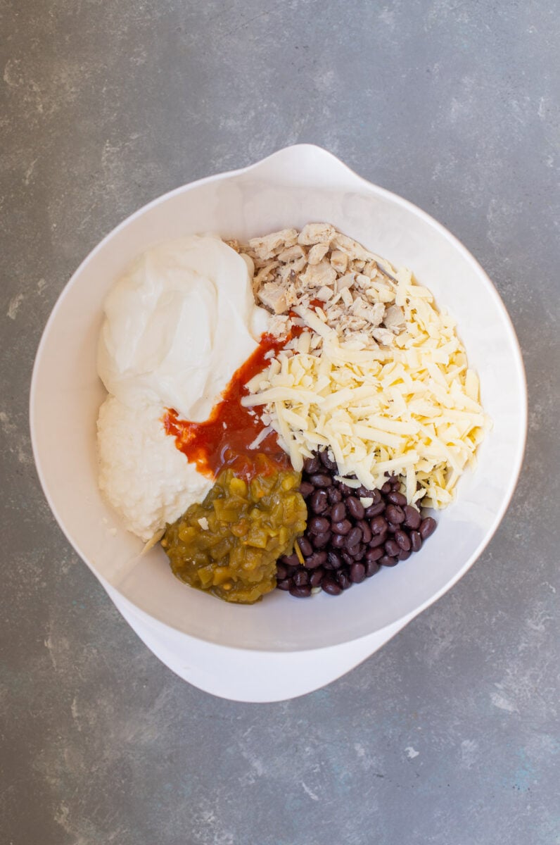 Ingredients for chicken enchilada dip in a large bowl before being mixed together.