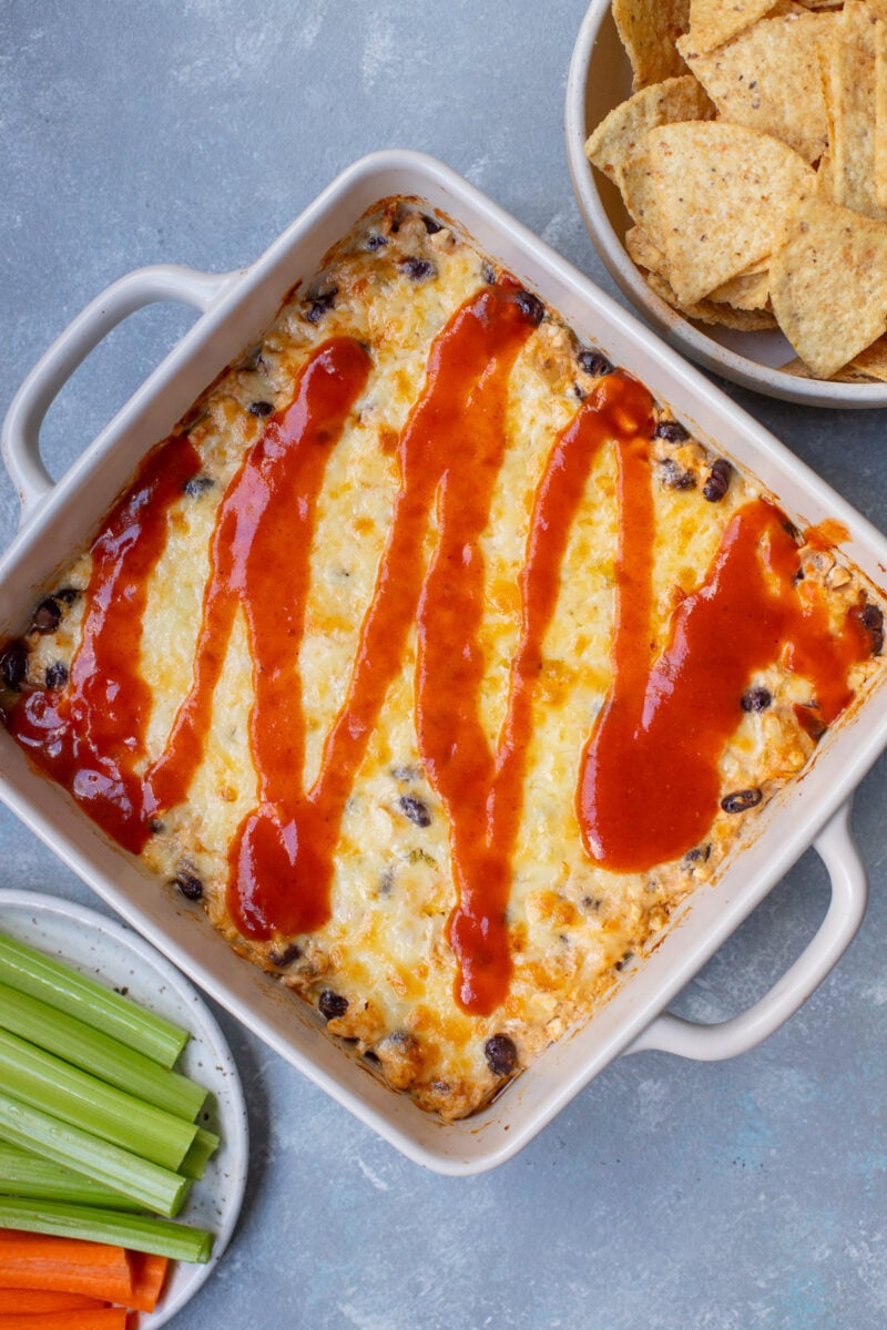 Chicken Enchilada Dip in a baking dish topped with more enchilada sauce and a bowl of chips on the side.