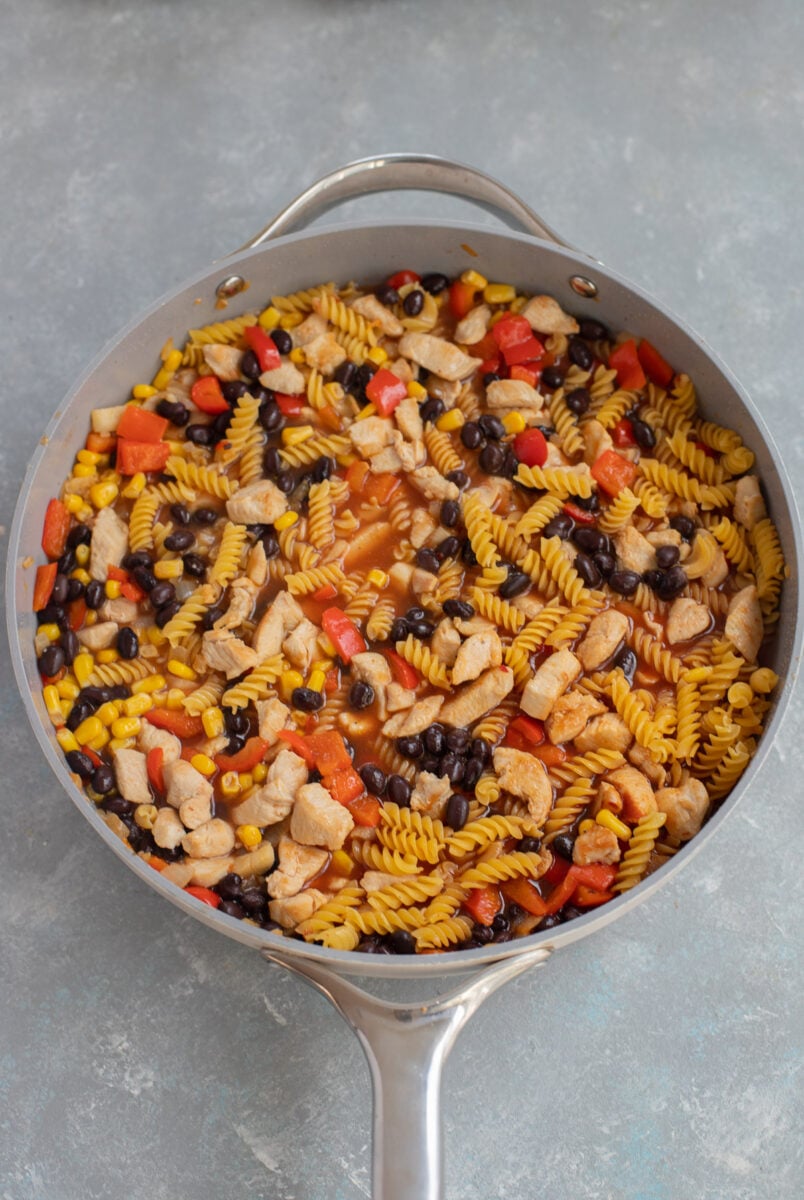 Uncooked chicken enchilada pasta stirred together in a skillet.