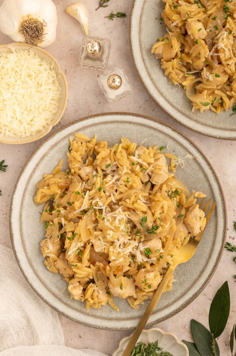 French Onion Orzo on a plate with a fork resting on the plate and another plate on the side.