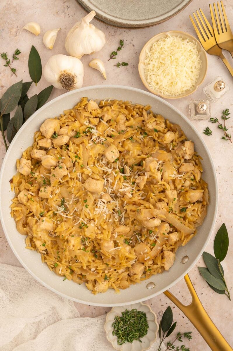 French onion orzo in a skillet with garlic, onion, and other ingredients on the side.