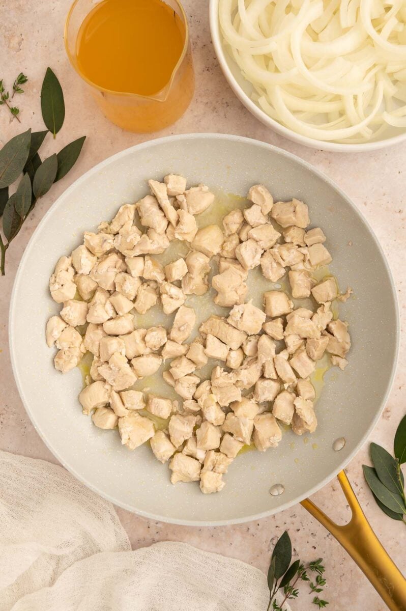 Chicken pieces in a skillet for one pot french onion orzo.