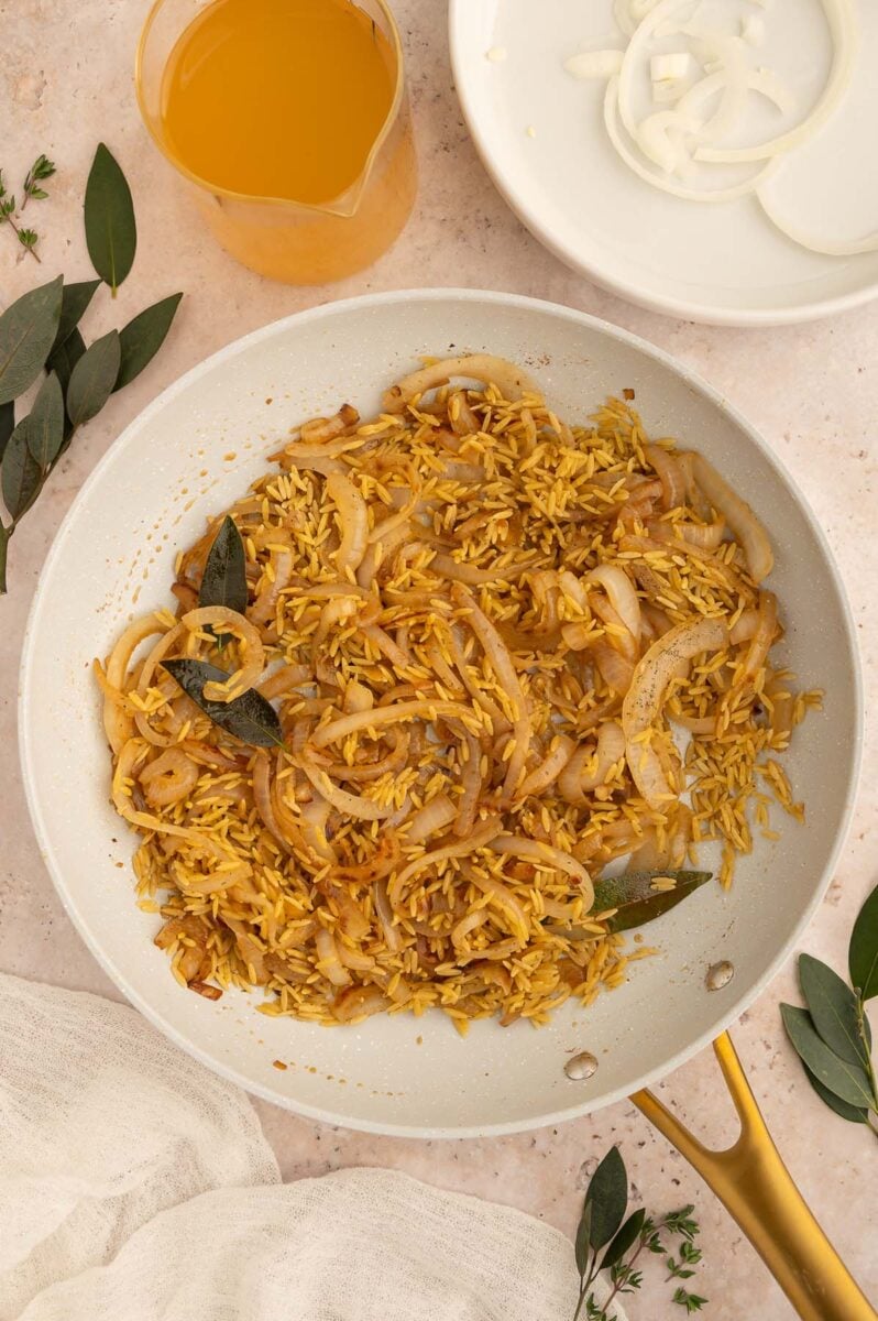 Onions, spices and orzo in a skillet cooking to make french onion orzo.