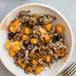 A serving of Ground Beef Butternut Squash on a white plate with a fork and blue towel on the side.