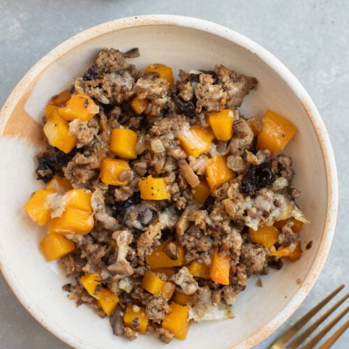A serving of Ground Beef Butternut Squash on a white plate with a fork and blue towel on the side.