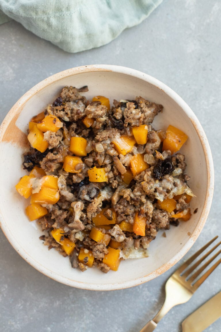 A serving of Ground Beef Butternut Squash on a white plate with a fork and blue towel on the side.