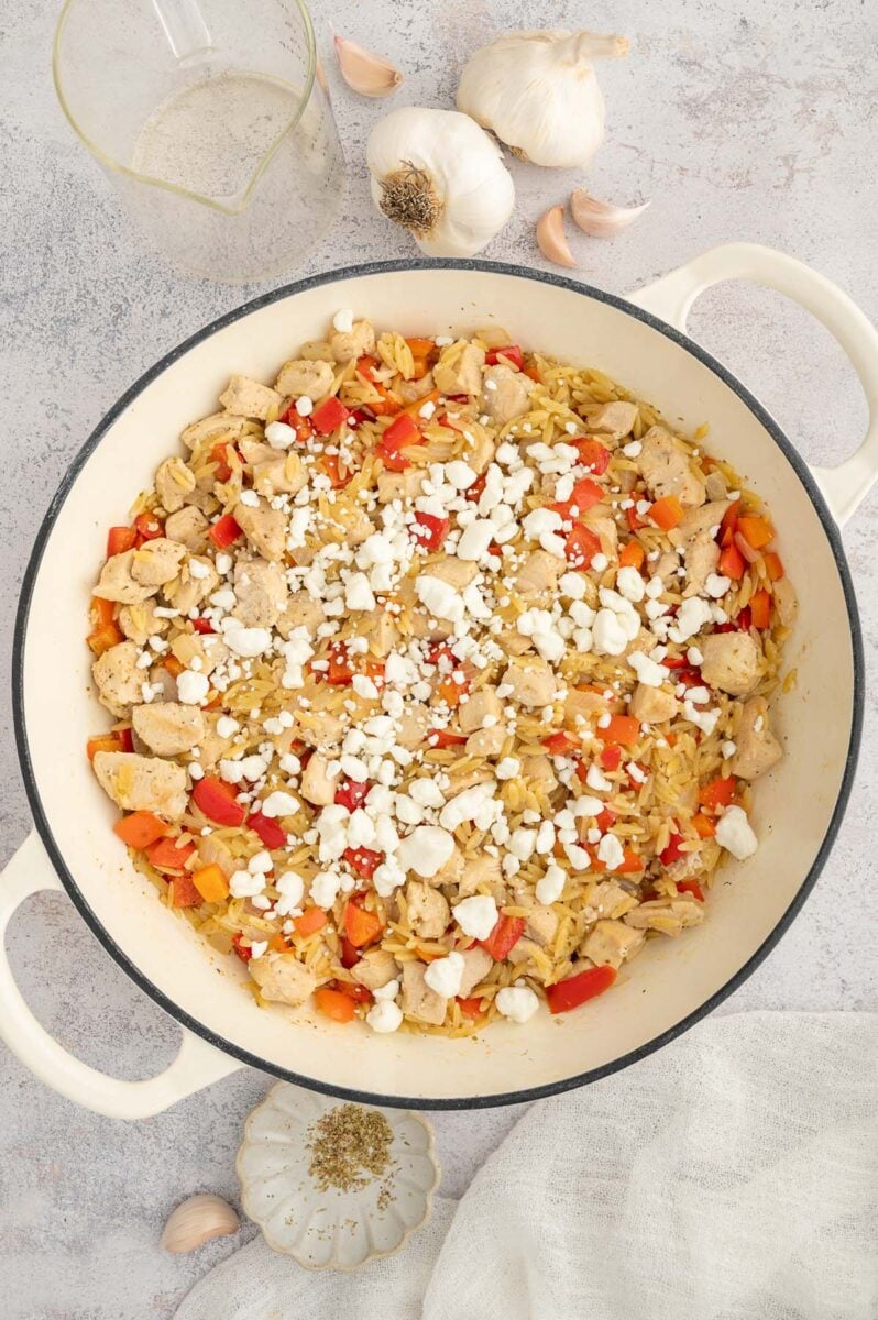 Red pepper chicken orzo topped with goat cheese before stirring together in a dutch oven.