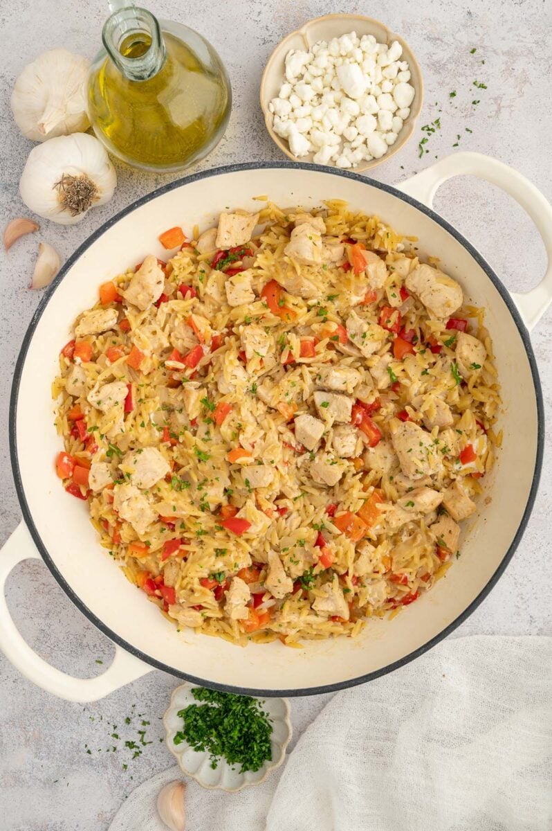 Red pepper chicken orzo in a dutch oven with a bowl of goat cheese on the side.