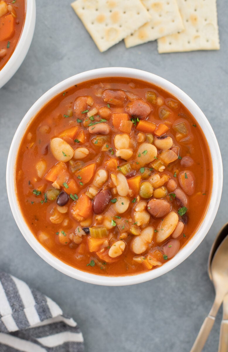 an overhead shot of a bowl of 15 bean soup with spoons on the side on a grey background