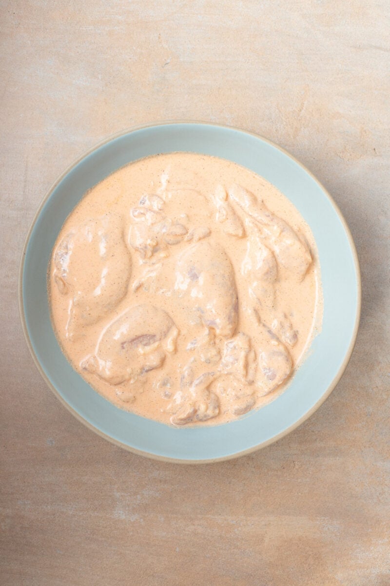 Uncooked chicken thighs in a bowl tossed in a greek yogurt marinade.