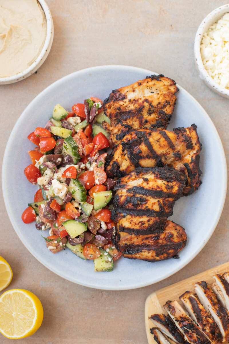 Grilled Greek Yogurt Marinated Chicken Thighs on a plate with a greek salad on the side. 
