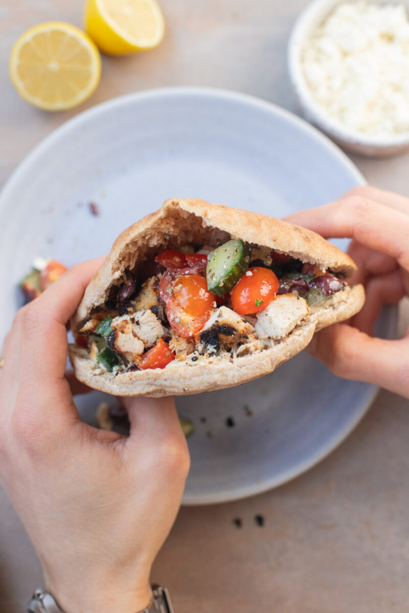 Hands holding a pita stuffed with greek yogurt marinated chicken and tomatoes and cucumbers. 
