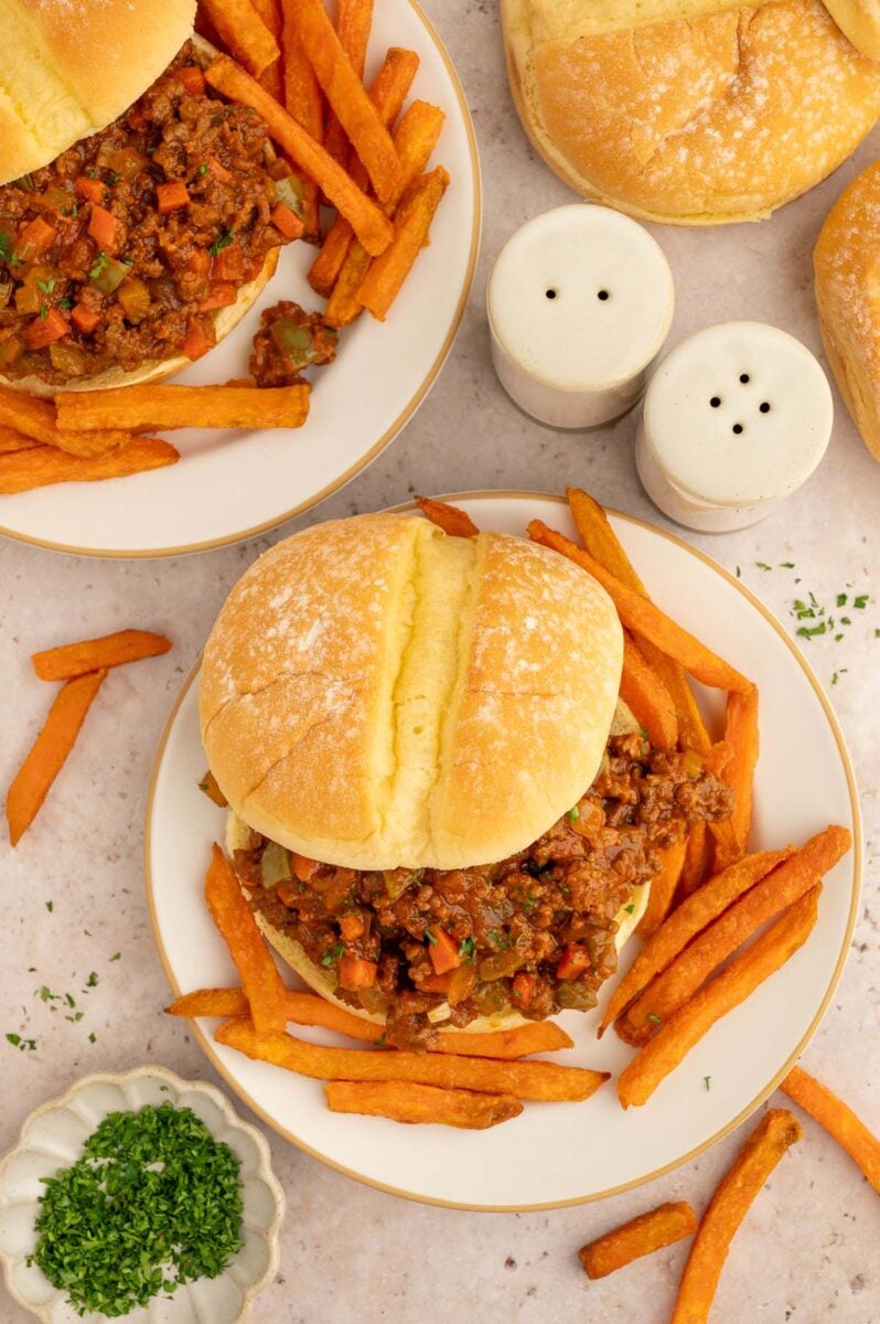 An overhead shot of healthy sloppy joe sandwiches on two plates with sweet potato fries on the plate. 
