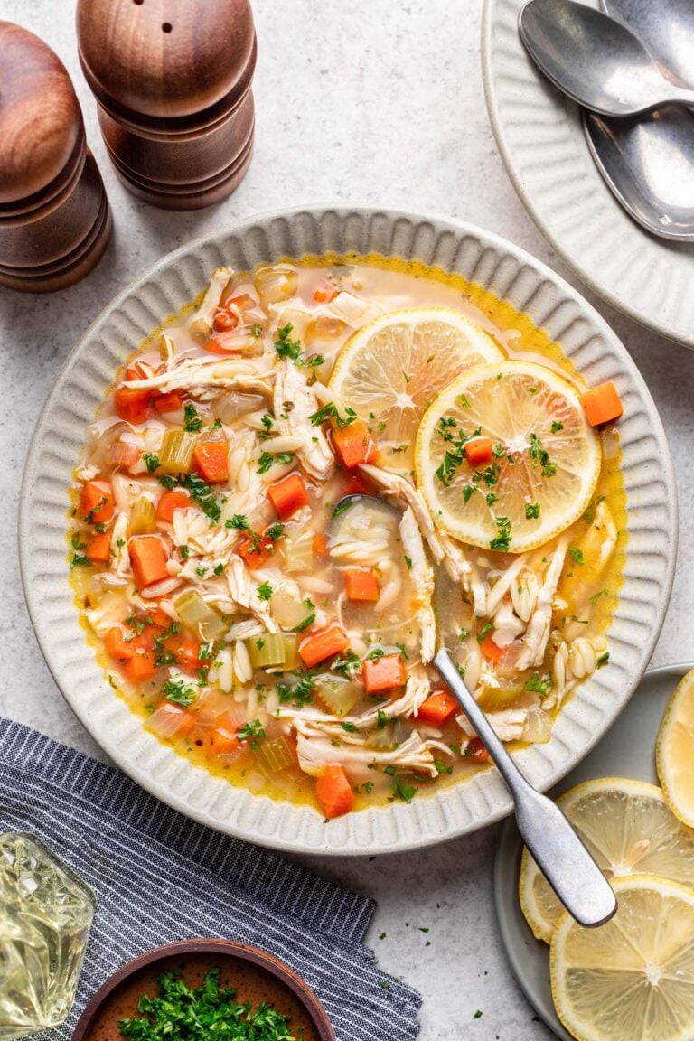 Lemon Chicken Soup in a white bowl with a spoon in it and garnished with lemon slices.