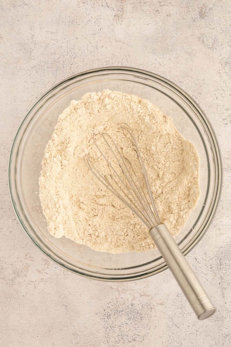 Dry ingredients for apple protein muffins in a glass large bowl with a whisk in it.
