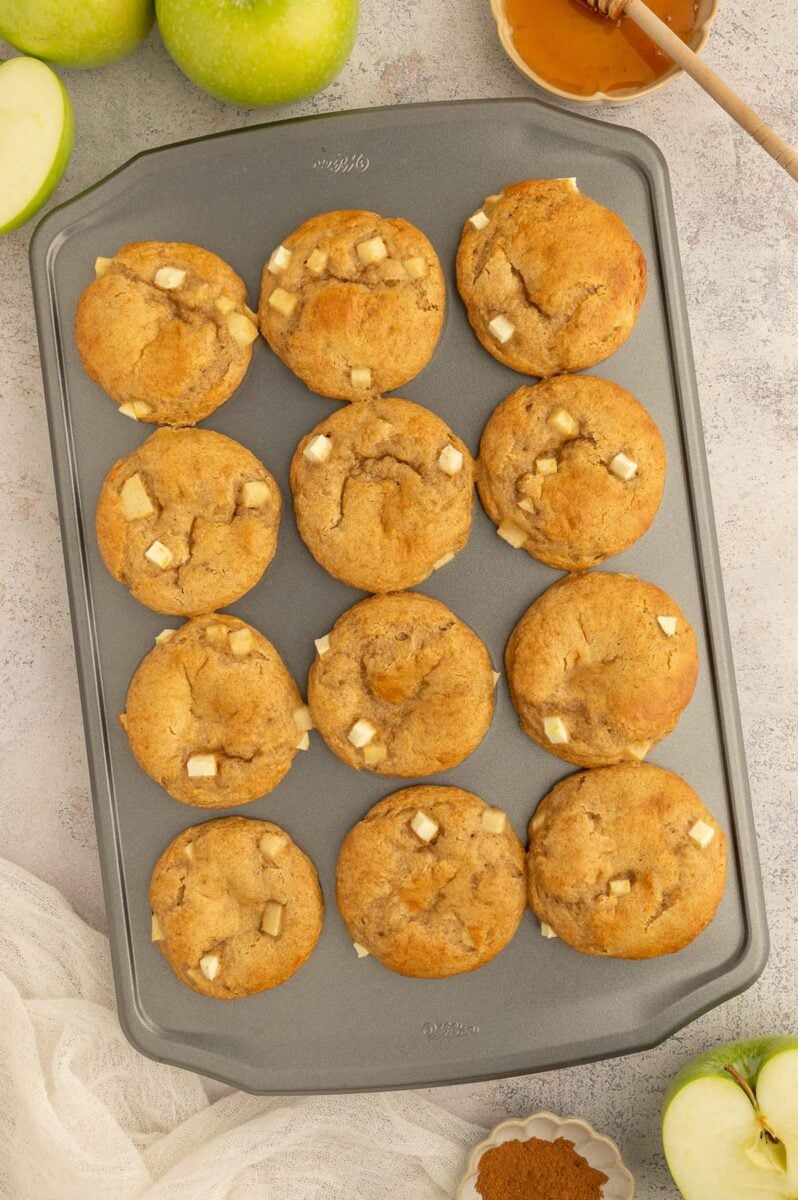 Apple Protein muffins fresh out of the oven with other apples on the side.