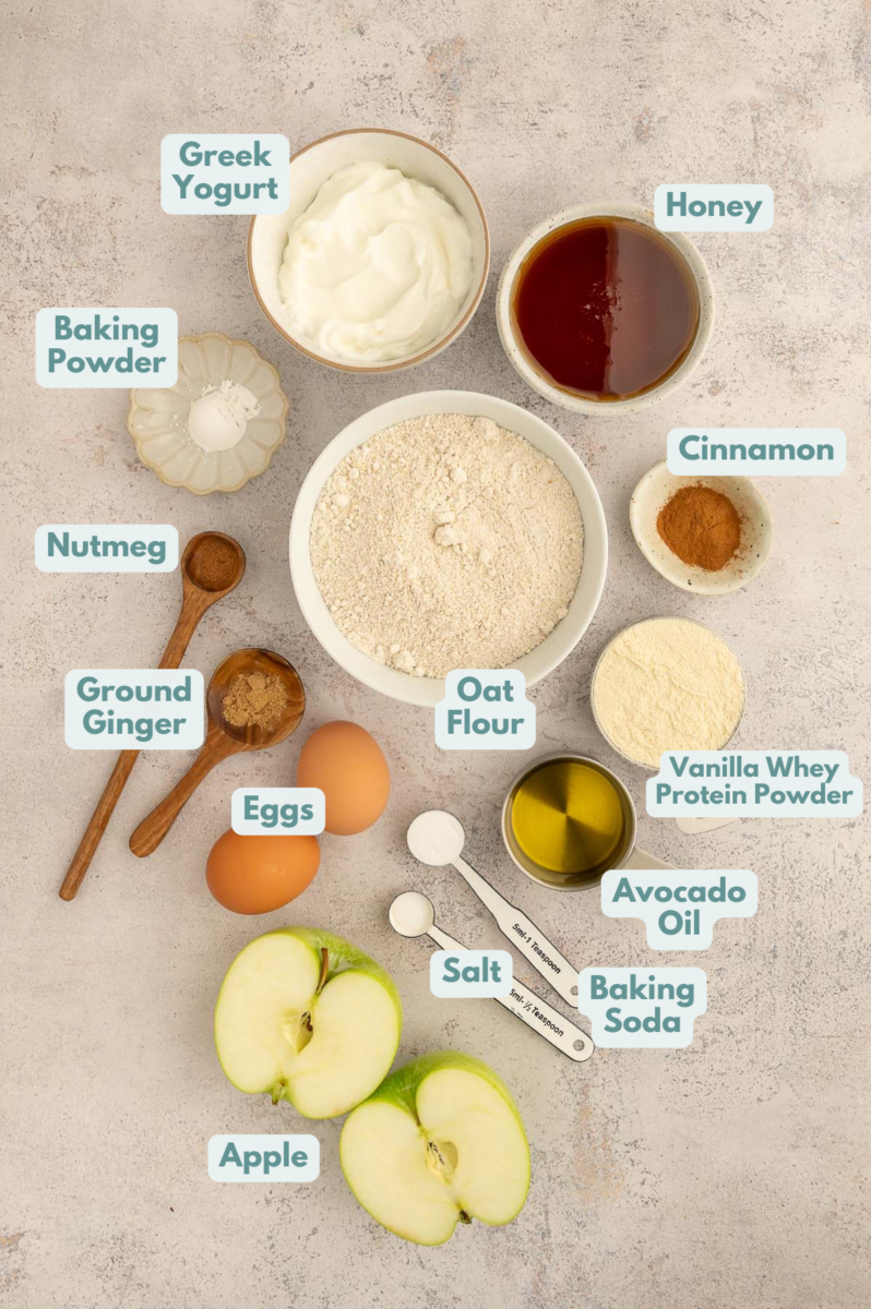 Labeled ingredients for Apple Protein Muffins in small white bowls on a grey background.