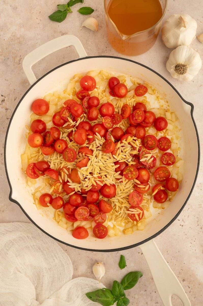 Onion, garlic, cherry tomatoes, and uncooked orzo in a skillet.