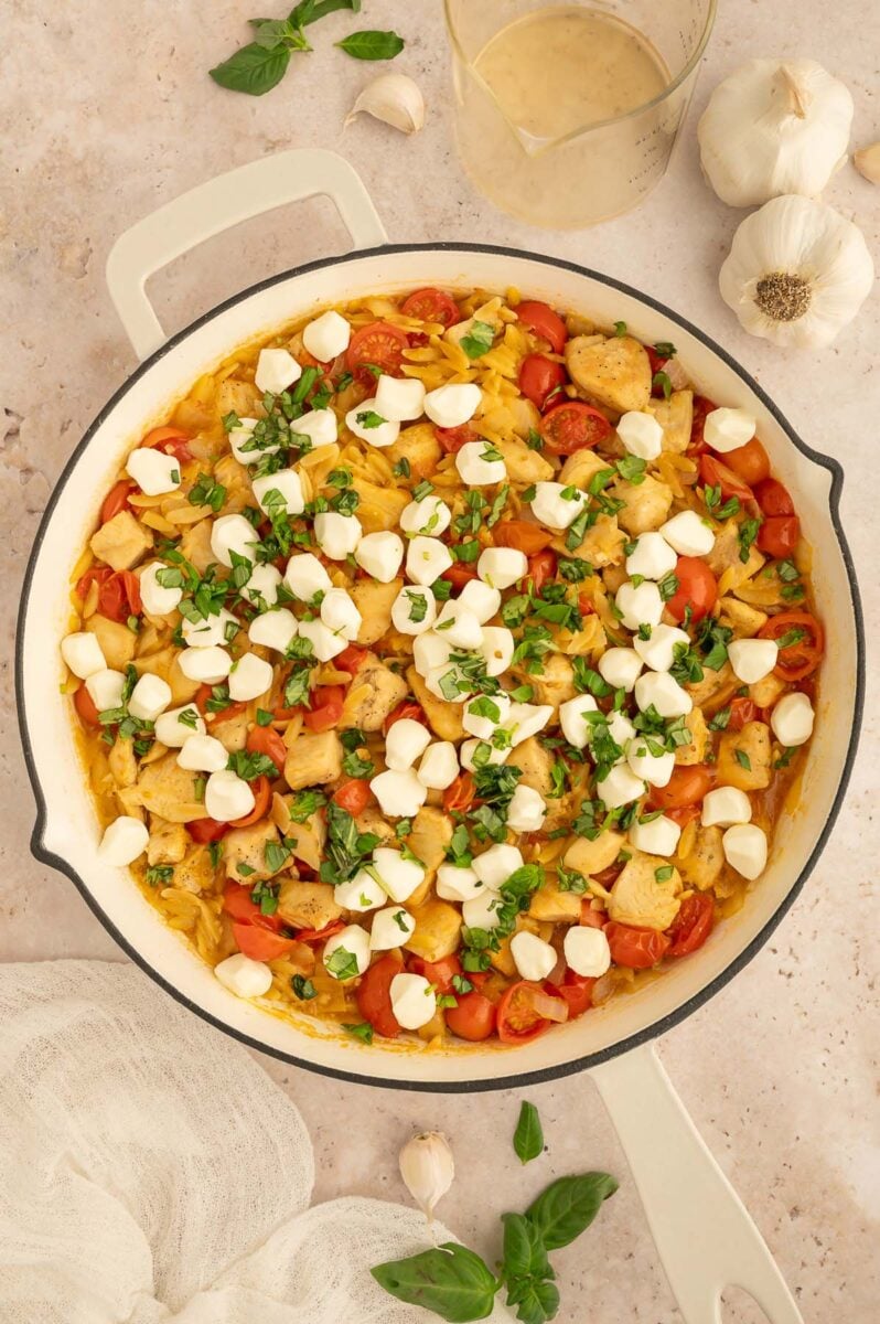 Chicken Caprese Orzo in a skillet topped with mozzarella pearls and fresh basil pieces. 