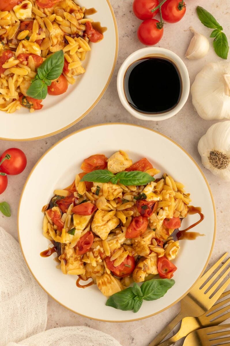 Two plates of chicken caprese orzo with a small bowl of balsamic glaze on the side. 