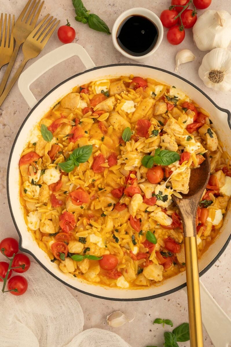 A wooden spoon in a pan of chicken caprese orzo.
