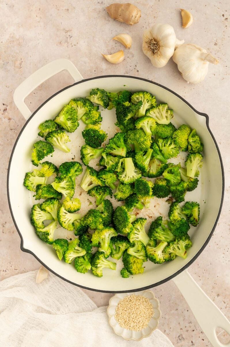 Sauteed broccoli florets in a pan with garlic cloves on the side.